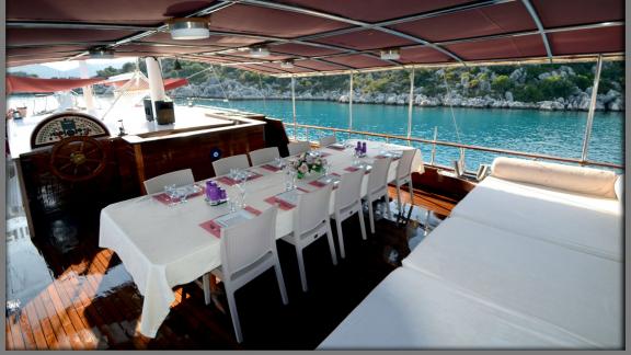 Gemütlicher Essbereich an Bord mit Blick auf das türkisfarbene Wasser und die Küste von Fethiye.