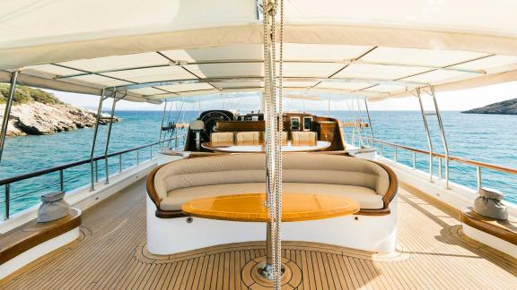 Main deck of the Gulet Caner 4 with covered seating area, wooden table and panoramic view of the sea and rocks.