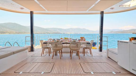 Set dining table on the aft terrace of the Genny catamaran, overlooking the sea and surrounding mountains.