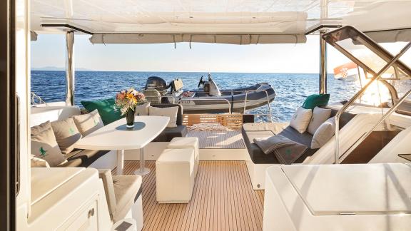 Cozy seating area with a dining table and flowers on a catamaran, overlooking the sea and a tender boat.