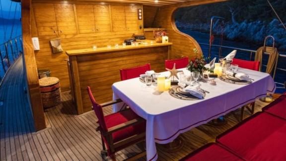 Elegant dining table on the deck of a yacht, illuminated by candles, with a wooden kitchen in the background.