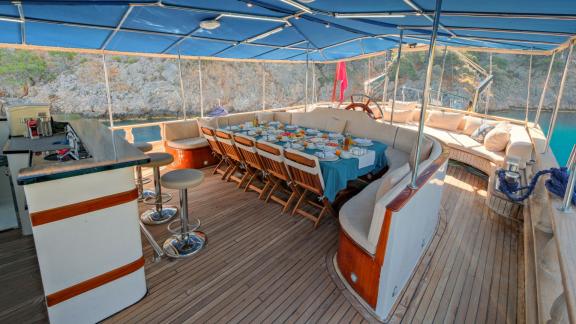 The covered dining area on the Gulet Tarkan 5, with a long, laid table, bar stools and comfortable seating.