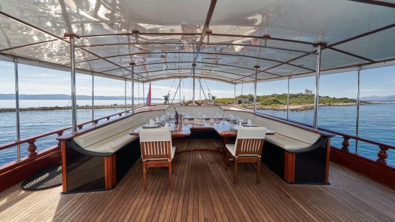 Elegant dining deck of a sailing yacht with covered area, set table and comfortable seating, overlooking calm waters and