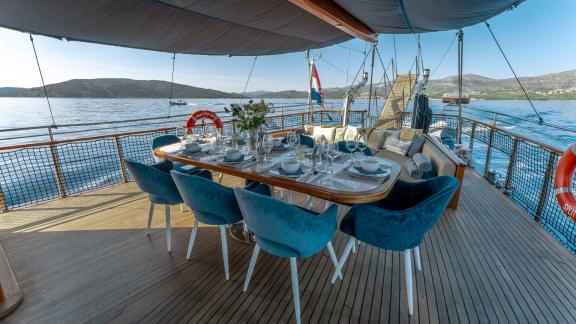 An elegantly laid dining table on the deck of the gulet Smart Spirit, with a view of the sea and the surrounding coastli