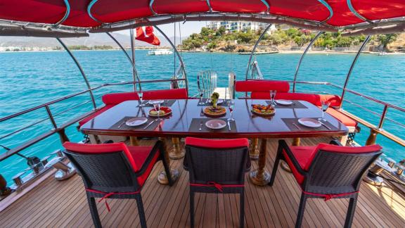 Dining area on the deck of Gulet Lycian Sirius, set table under red sunshades with views of the sea and coastline.