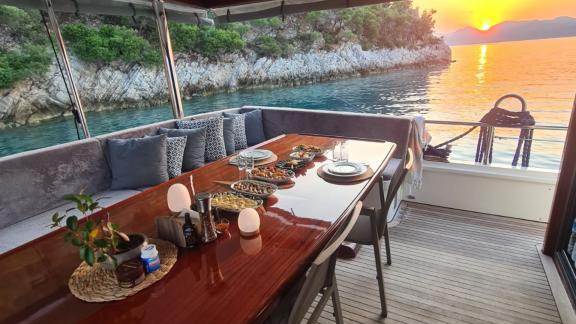 A set dining table on the gulet, surrounded by scenic cliffs and a breathtaking sunset over the sea.