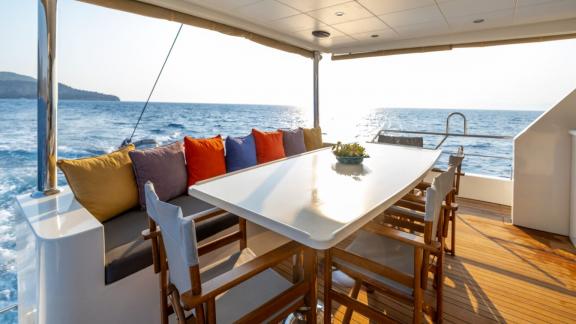 The aft deck of trawler yacht Kaan Bey 2 features a spacious dining area with a sea view.