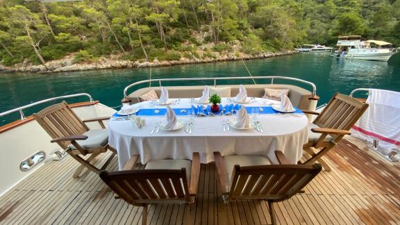 Offener Essbereich auf dem Achterdeck der Motoryacht Ser 1 mit Blick auf Wald und Meer.