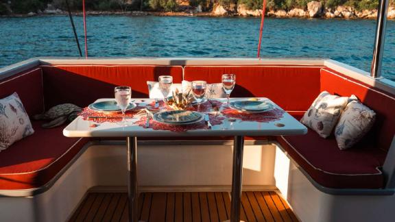 Comfortable red cushions and dining table on open deck of Barbaros 3 lobster yacht.
