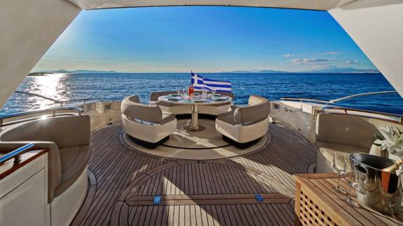 Auf dem Achterdeck der Sea U Motoryacht stehen ein runder Tisch und bequeme Sessel, während die griechische Flagge weht.
