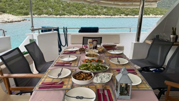 The aft deck of Sveti Sky features a dining table set against the sea with surrounding seating.