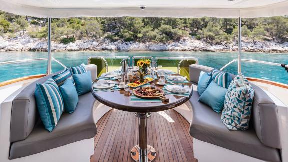 The aft deck of Dream motor yacht in Athens shows a round dining table set with food and sea view.