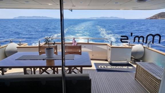 At Athens coast aft deck of Mammas motor yacht with dining table and seating area facing the sea.