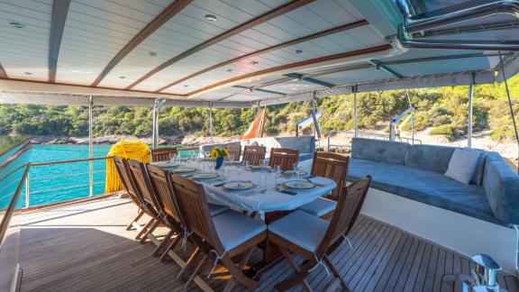 В Бодруме аренда гулета Giulia на корме стол для еды и зона отдыха с видом на море.