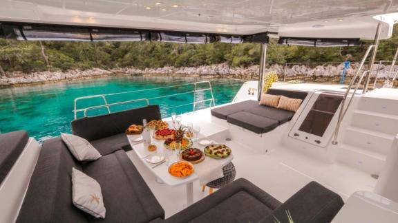 The outdoor area of the Daphne catamaran features a stylish lounge with a set dining table, surrounded by turquoise wate