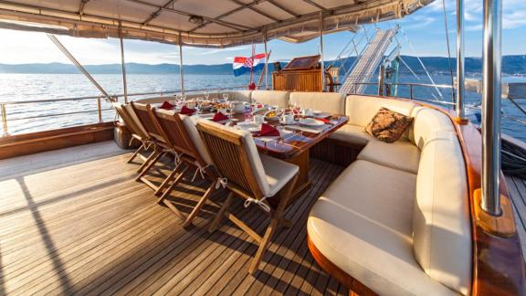 Set dining table on the deck of a gulet with the Croatian flag in the background, surrounded by calm sea.