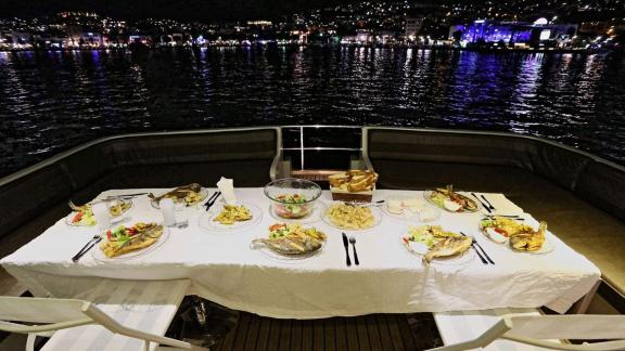 Juliet motoryatının güvertesinde, Bodrum'un gece manzarasında lezzetli bir akşam yemeği sunuluyor.