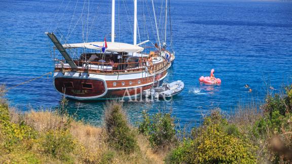 Gulet Allure, yeşil bitki örtüsüyle çevrili, kristal berraklığında suya sahip sakin bir koyda demirlemiştir