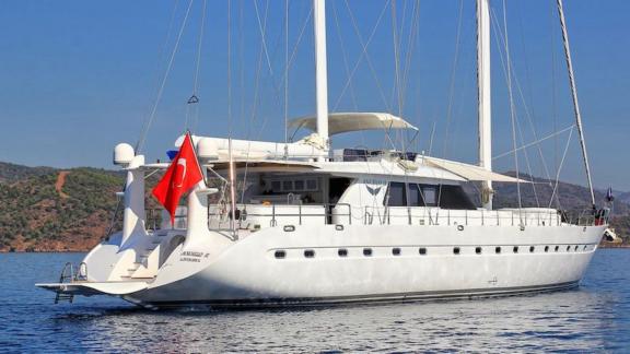 Die Angelo 2 Motorsailer-Yacht liegt vor Anker in einer ruhigen Bucht auf blauem Wasser, die türkische Flagge weht.