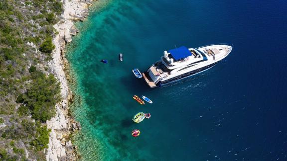 The motor yacht Agave is anchored in turquoise waters, surrounded by water sports equipment.