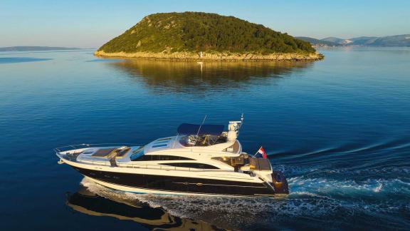 The motor yacht Agave cruises in calm waters past a green island.