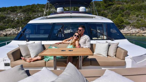 A couple relaxes on the deck of the motor yacht Agave in a serene bay.