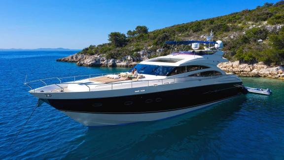 The motor yacht Agave anchors in crystal-clear waters by a green coastline near Split, Croatia.