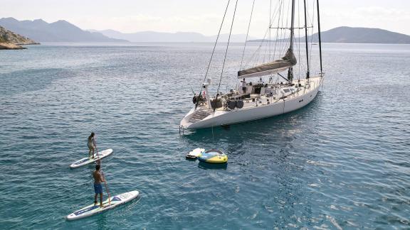 Die Luxusyacht Aizu liegt vor Anker in Griechenland, Gäste genießen Paddleboard und Wasserspielzeug.