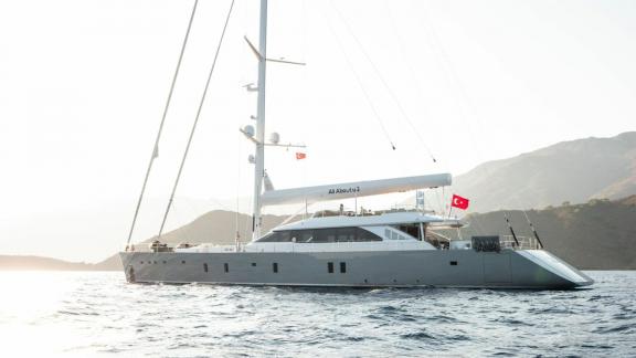 Моторный парусник All About U 2 на фоне живописных гор при закате.