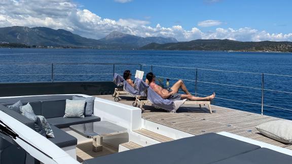 Two people relaxing on sun loungers aboard the Catamaran Alteya, enjoying stunning views of the sea and mountains.