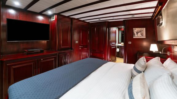 In Göcek gulet charter option Always Smile master cabin with large bed tv unit and bathroom access visible.