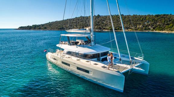 The Catamaran Amada Mia is anchored in crystal-clear, turquoise waters off the Adriatic coast of Croatia, while two peop