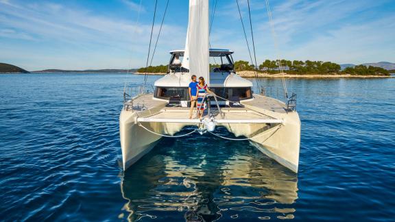 The Catamaran Amada Mia is anchored in calm waters off the Adriatic coast, with two people enjoying the view.