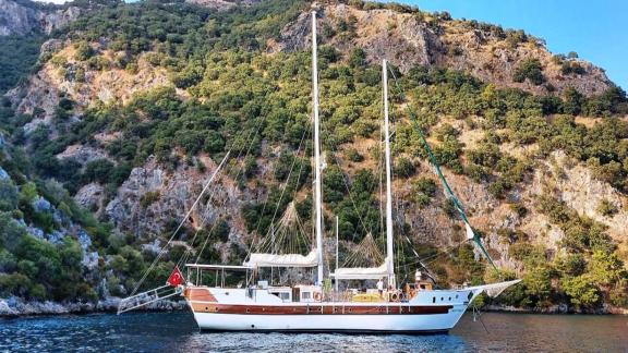 The gulet yacht Amazon Solo is moored off a picturesque coast in Turkey, surrounded by green hills and clear water.