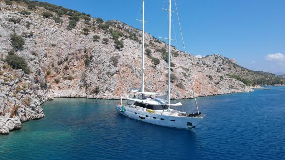 Motorsailer Angelo 3 anchored quietly in a rocky cove, surrounded by blue waters.