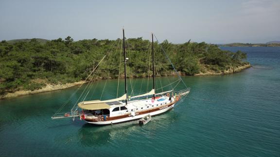The Gulet Life is Life is anchored in a tranquil bay near Bodrum, surrounded by green hills and clear waters.