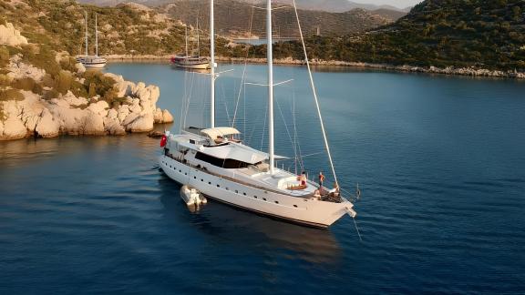 The yacht Angelo 2 is anchored in a calm bay surrounded by rocky cliffs.