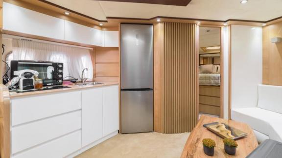 Die Motoryacht Aron 26 verfügt über eine elegante Küche mit weißen Schränken, großem Kühlschrank und Mikrowelle.