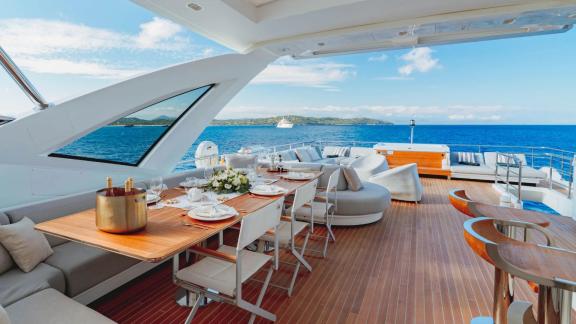 The upper deck of motor yacht Nemesis features a dining table and spacious seating for ocean enjoyment.