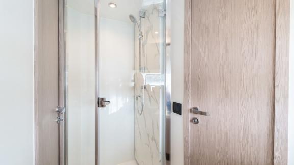 Glass door and marble-effect walls create a sleek and minimalistic shower design.