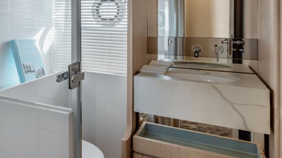 Das Badezimmer bietet ein Waschbecken in Marmoroptik, einen großen Spiegel und eine Glasdusche.