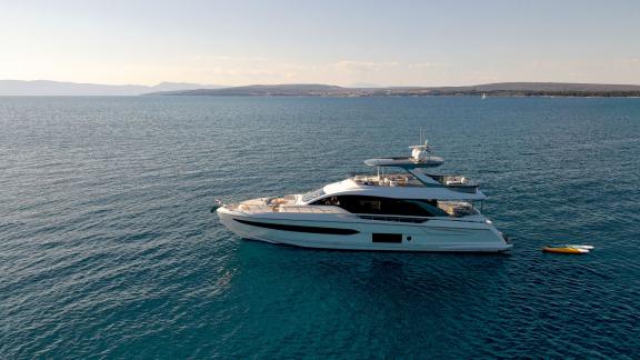 Die Omr Group ankert im ruhigen Meer. Neben der Yacht treibt ein Paddleboard.