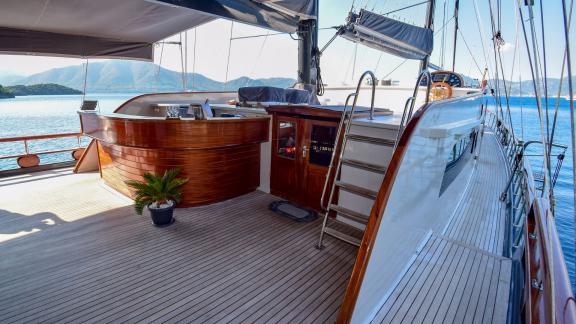 The deck of the gulet 'Ugur' with a bar and a ladder, against a picturesque sea and mountain backdrop.