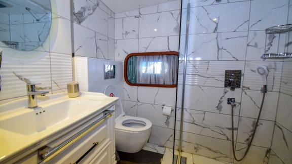 A modern bathroom on the gulet 'Ugur' with marble walls, a shower and a small window.