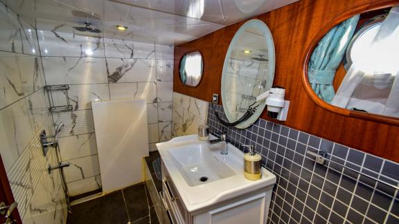 A modern bathroom on the gulet 'Ugur' with marble walls, an oval mirror and a small window.