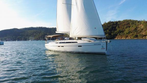 Sailing yacht Santiago cruising on the sea with green scenery in the background.