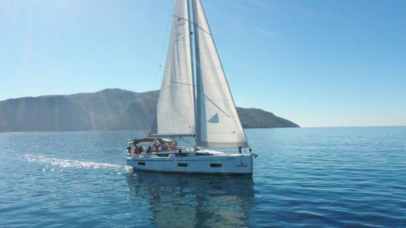 Die Segelyacht Fiesta segelt ruhig auf dem Meer, im Hintergrund sind grüne Berge zu sehen.