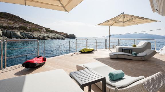 Sun deck of a yacht with views of the sea and coastline. Sun loungers, seating furniture, sun umbrellas, and water scoot