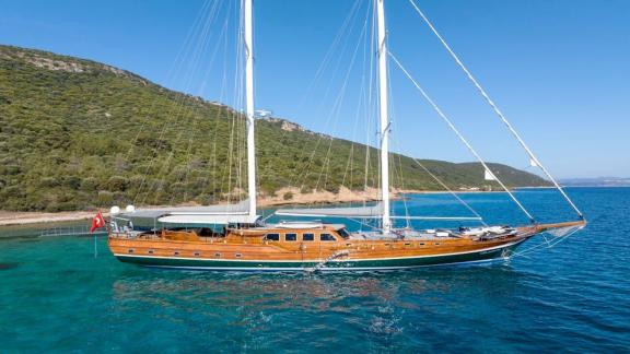 The gulet Bedia Sultan lies majestically in the turquoise waters off the coast of Bodrum, surrounded by green hills.