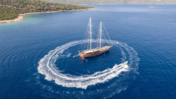 The gulet Bedia Sultan from Bodrum, orbited by a boat that creates a swirl of water in the deep blue sea.